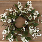 Floral wreath with white flowers and green leaves on a wooden surface