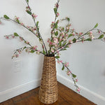 Wicker vase with cherry blossom branches against a white wall.