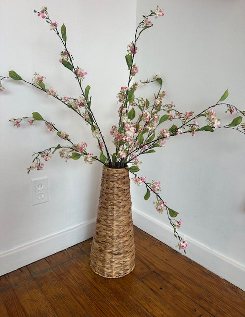 Wicker vase with cherry blossom branches against a white wall.
