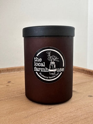 Brown travel mug with a black lid and 'the local farmhouse' logo on a wooden surface.