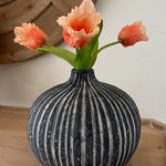 Decorative vase with striped pattern on a wooden surface, containing peach-colored flowers.