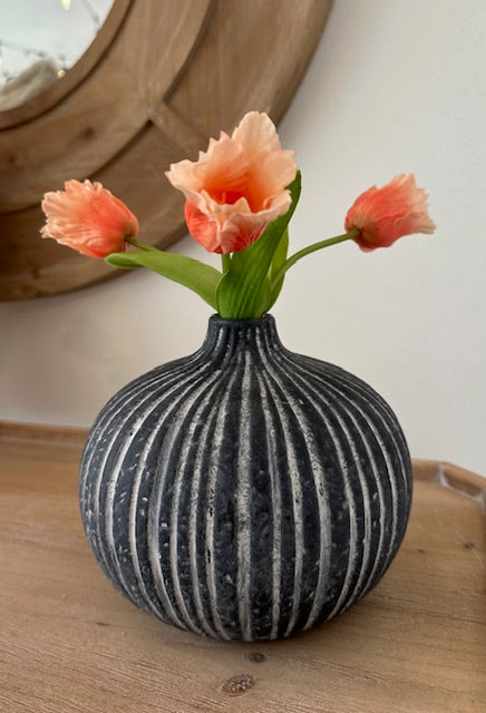 Decorative vase with striped pattern on a wooden surface, containing peach-colored flowers.