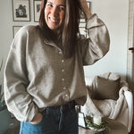 Woman in a gray sweater and blue jeans standing in a living room.
