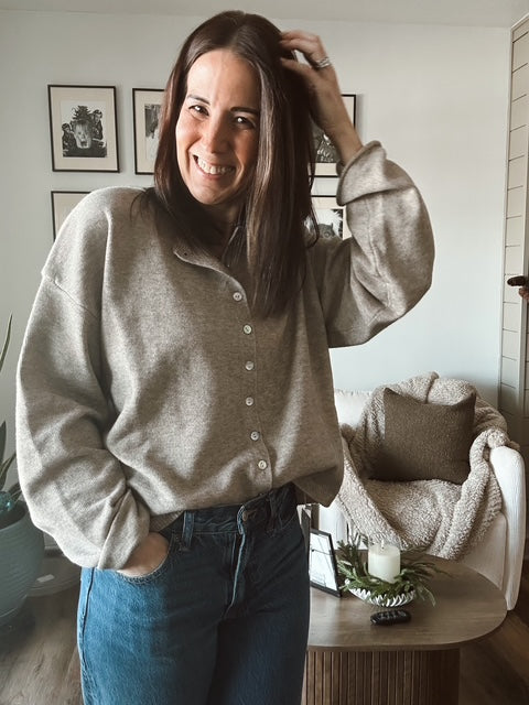 Woman in a gray sweater and blue jeans standing in a living room.