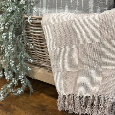 Textured blanket with fringe draped over a wicker chair on a wooden floor.