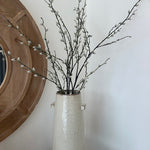 Decorative vase with willow branches against a white wall
