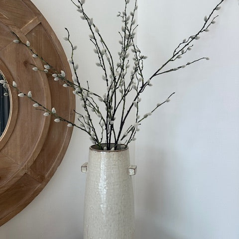 Decorative vase with willow branches against a white wall