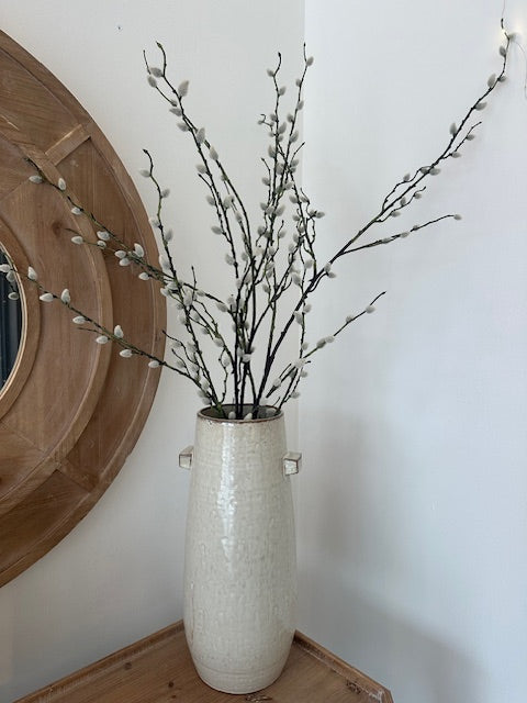 Decorative vase with willow branches against a white wall