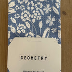 Kitchen tea towel with floral pattern and 'Geometry' label on a wooden surface