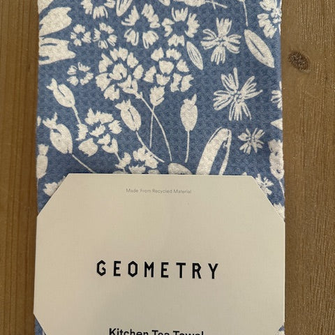 Kitchen tea towel with floral pattern and 'Geometry' label on a wooden surface