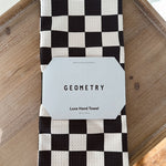 Black and white checkered hand towel with 'Geometry' label on a wooden surface
