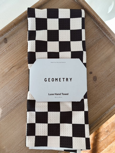 Black and white checkered hand towel with 'Geometry' label on a wooden surface