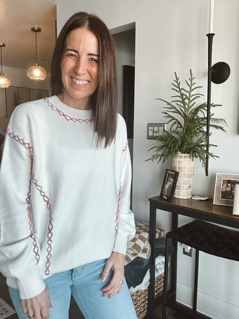 Woman wearing a white sweater with red patterns in a home setting