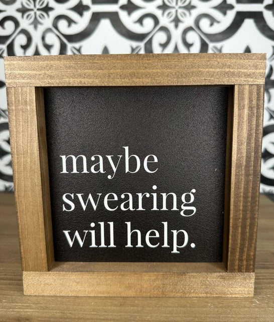 A wooden framed sign with a dark background displaying the text 'maybe swearing will help.' in white lettering.