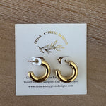 Gold hoop earrings on a Cypress Press Designs card with a wooden background