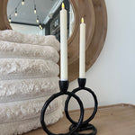 Decorative candle holder with black handles on a textured surface in front of a mirror.