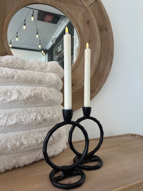Decorative candle holder with black handles on a textured surface in front of a mirror.