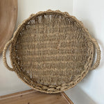 Round woven basket with handles on a light wooden surface