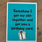 Blue birthday card with humorous text and a gift illustration on a wooden surface