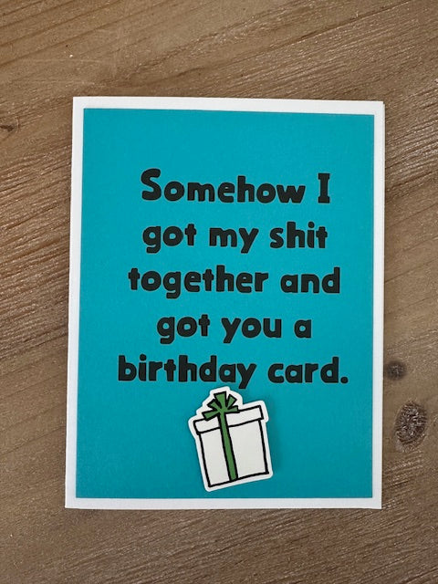 Blue birthday card with humorous text and a gift illustration on a wooden surface