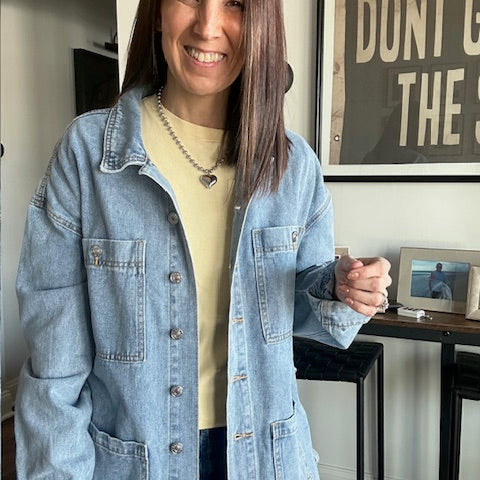 Woman wearing a light blue denim jacket indoors with a framed picture in the background.