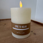 Candle labeled 'Time to Relax' on a wooden surface with a white background