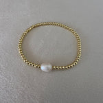 Gold bracelet with a pearl on a gray surface