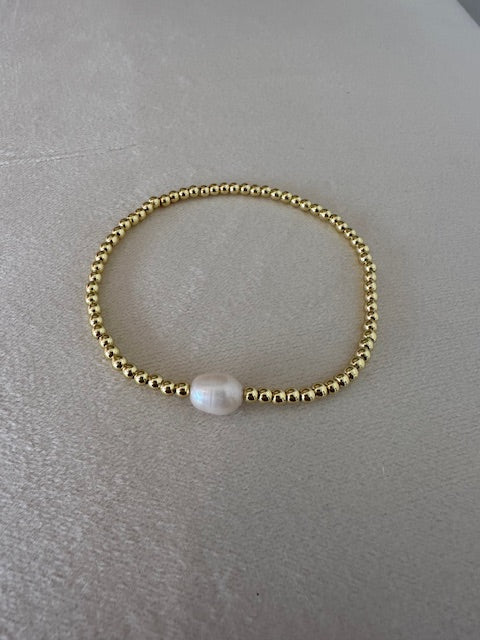 Gold bracelet with a pearl on a gray surface