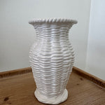 White textured vase on a wooden surface with a white wall background