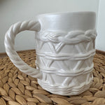 White ceramic mug with rope design on a woven mat