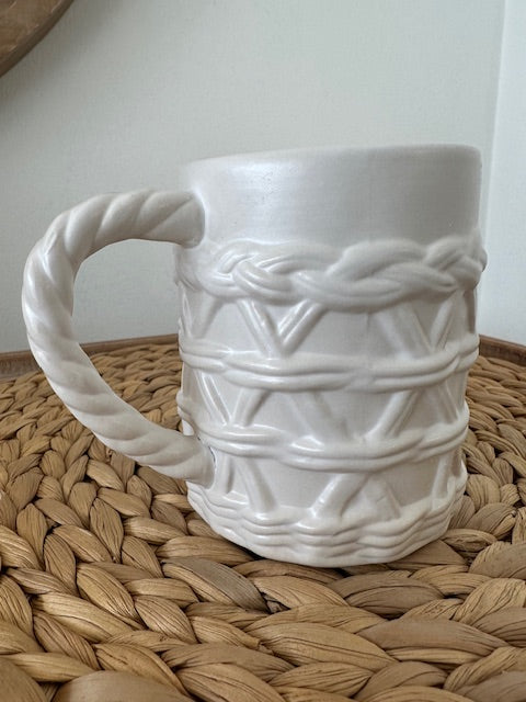 White ceramic mug with rope design on a woven mat