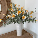 Artificial flower arrangement on a wooden surface with a white wall background