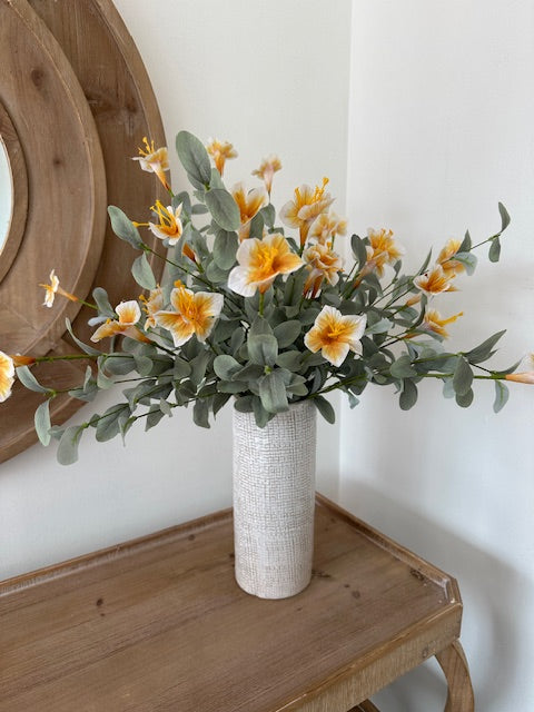 Artificial flower arrangement on a wooden surface with a white wall background