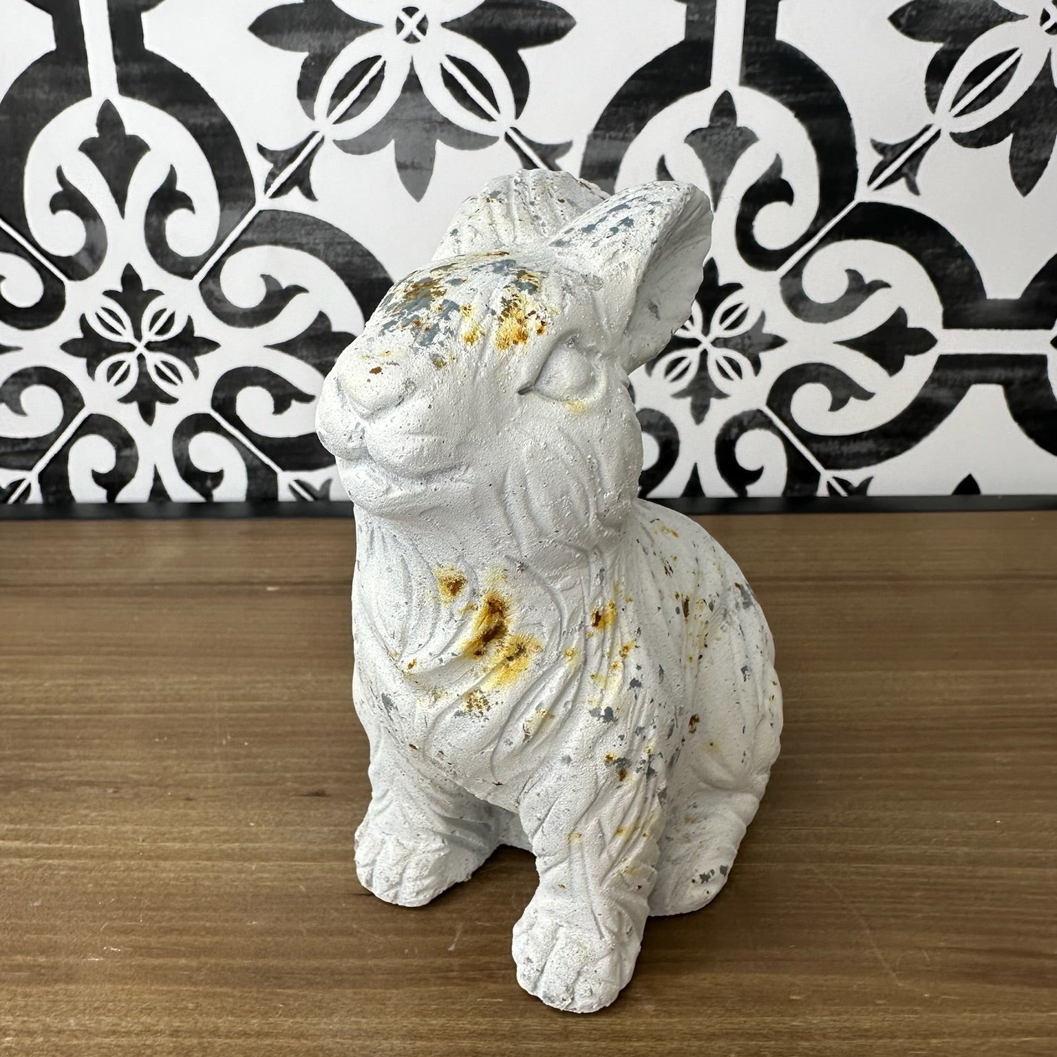 A white concrete rabbit statue with a textured coat and rustic distressed finish, featuring sporadic rusty accents.