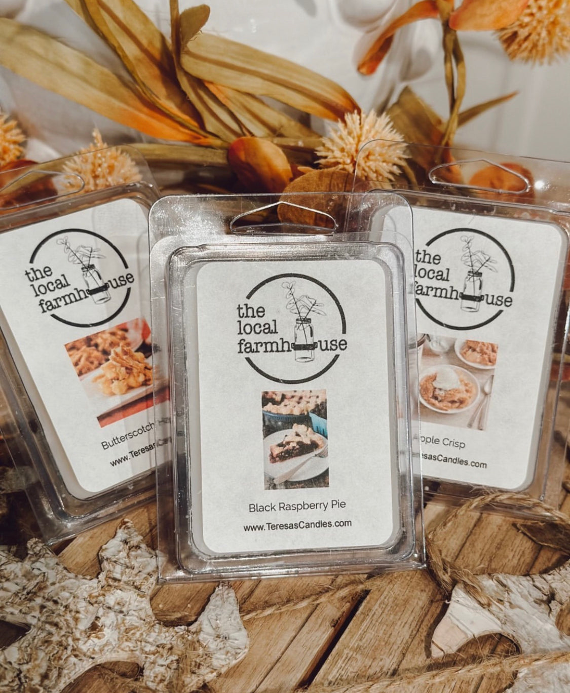 Three clear plastic packaging containers with the labels 'Local Farmhouse', 'Black Raspberry Pie', and 'Caramel Coffee' showing images of the fragrance oils used.