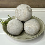 Three round washed wood decorative balls placed on a round ceramic plate, with a blurred background suggesting a home environment.