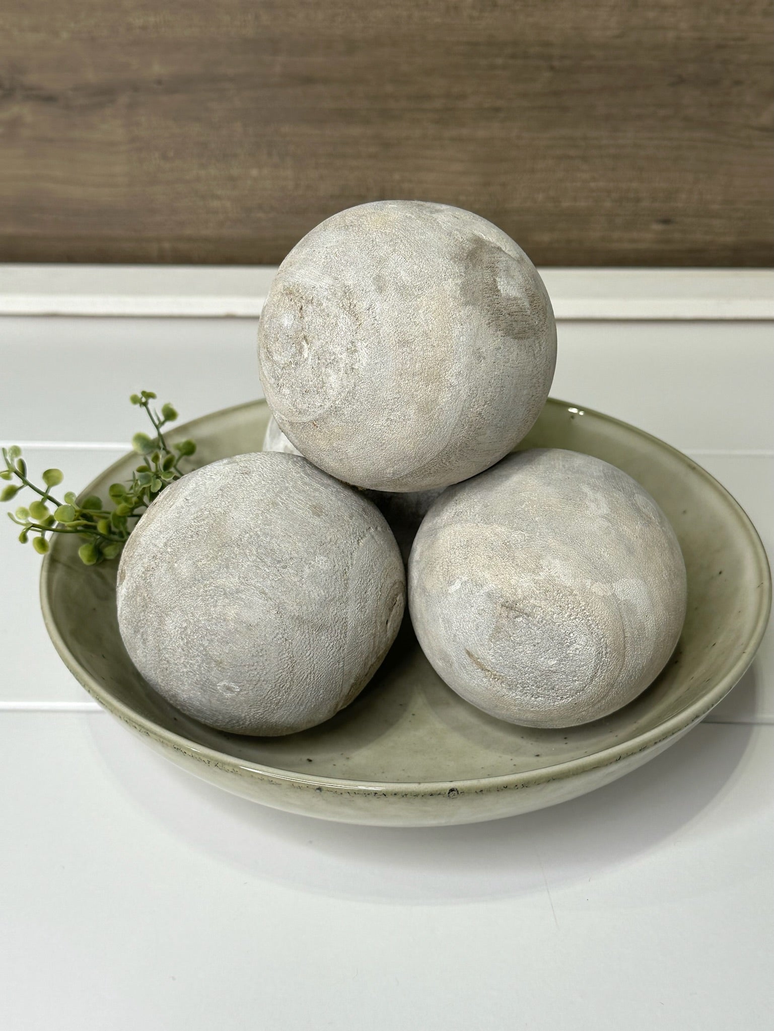 Three round washed wood decorative balls placed on a round ceramic plate, with a blurred background suggesting a home environment.