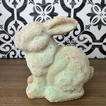 A weathered gray garden rabbit statue with a distressed finish, showing signs of wear.