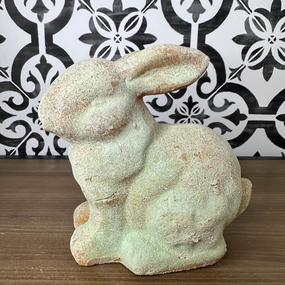 A weathered gray garden rabbit statue with a distressed finish, showing signs of wear.